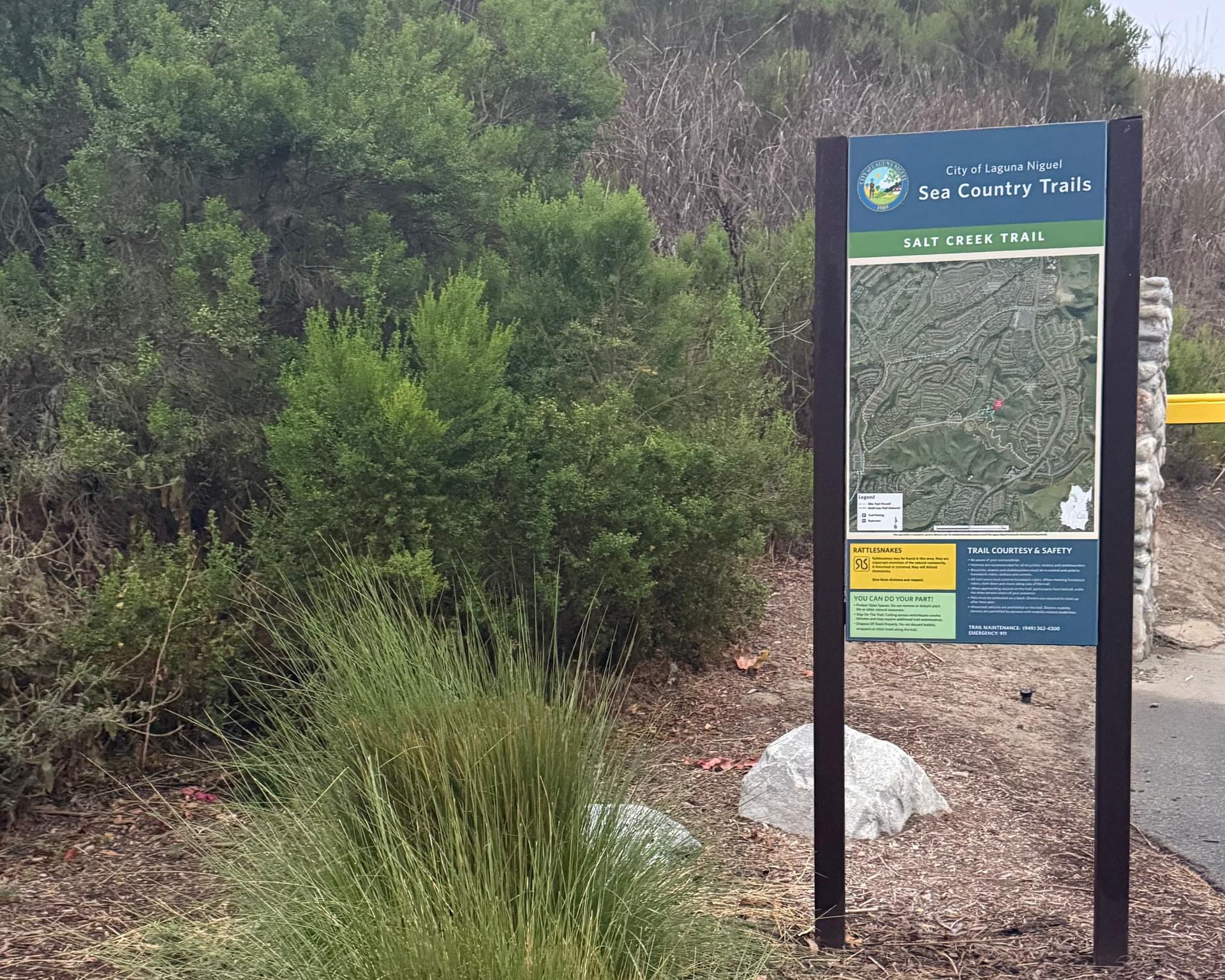 Trail sign in a natural setting with greenery and rocks